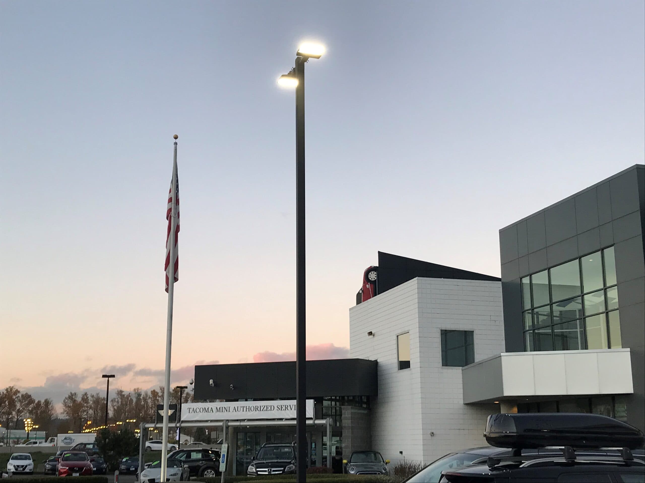 Pole-mounted LED area lights over a dealership parking lot at dusk